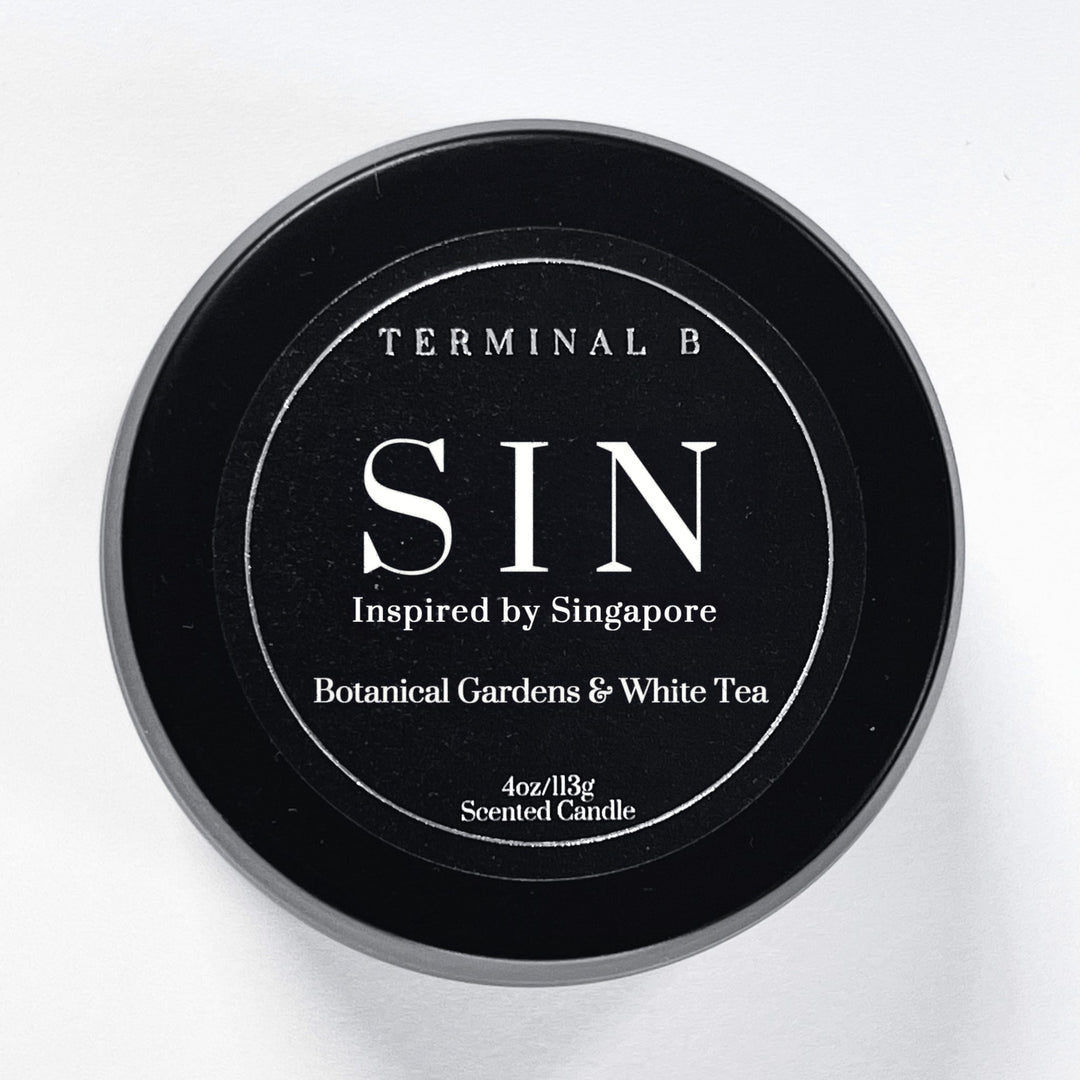 SIN 4oz Travel Tin candle by Terminal B. Botanical Gardens & White Tea fragranced and displayed against a white background. Inspired by Singapore, carefully designed for an elegant, long-lasting scent.