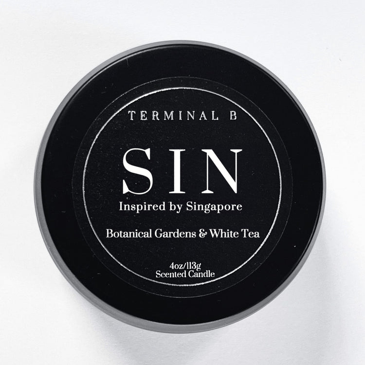 SIN 4oz Travel Tin candle by Terminal B. Botanical Gardens & White Tea fragranced and displayed against a white background. Inspired by Singapore, carefully designed for an elegant, long-lasting scent.